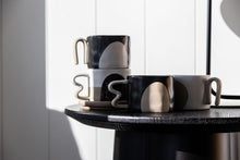 Load image into Gallery viewer, The Benni mug has unique handles that resemble the number 3. The mugs are a neutral colour scheme with shades of black, white and beige. The shape is uniform with the same diameter at top and bottom.
