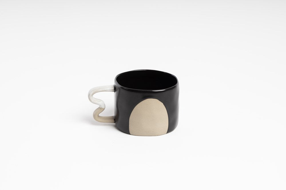 The black version of this mug is black with a white handle and has a large round beige shape.